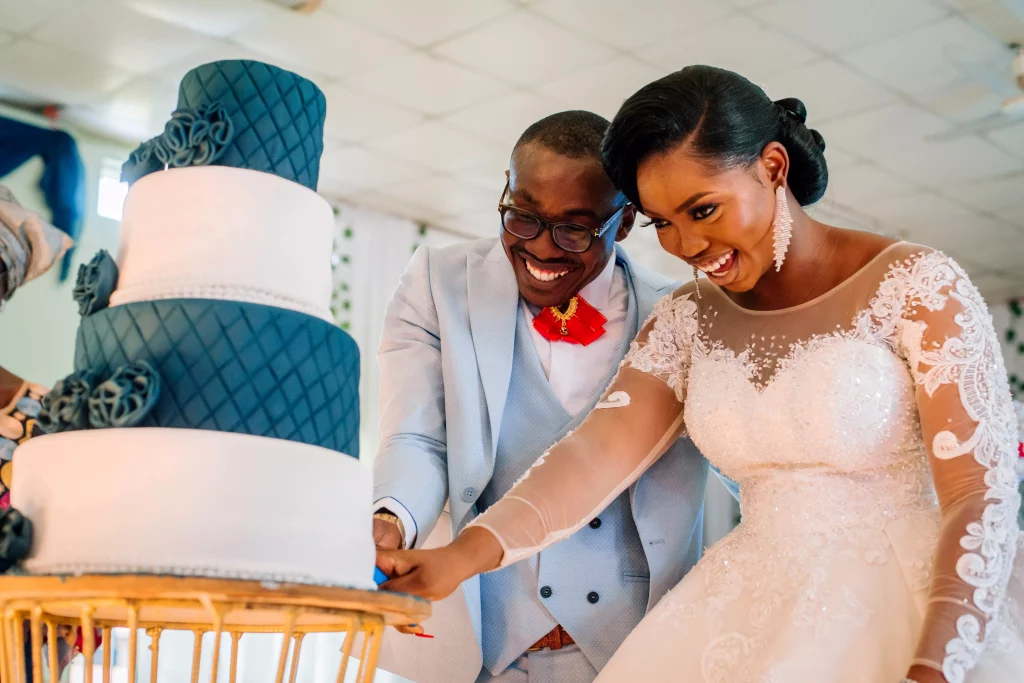 couple smiling while cutting wedding cake shot by photographer in lagos, Ash Robin