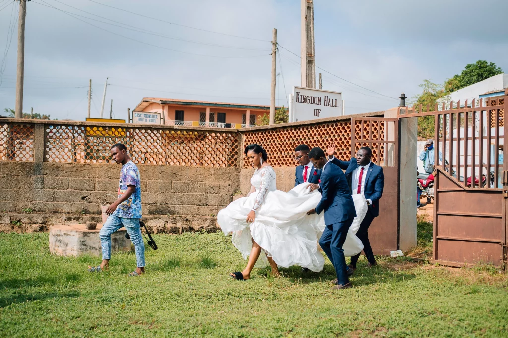 groomsmen helping bride with her wedding dress so she can easily walk at a nigerian wedding